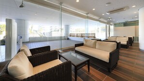 A modern indoor lounge area with wicker furniture, glass partitions, and large windows offering views of the outside. - Katsuura Hilltop Hotel & Residence (Katsuura)