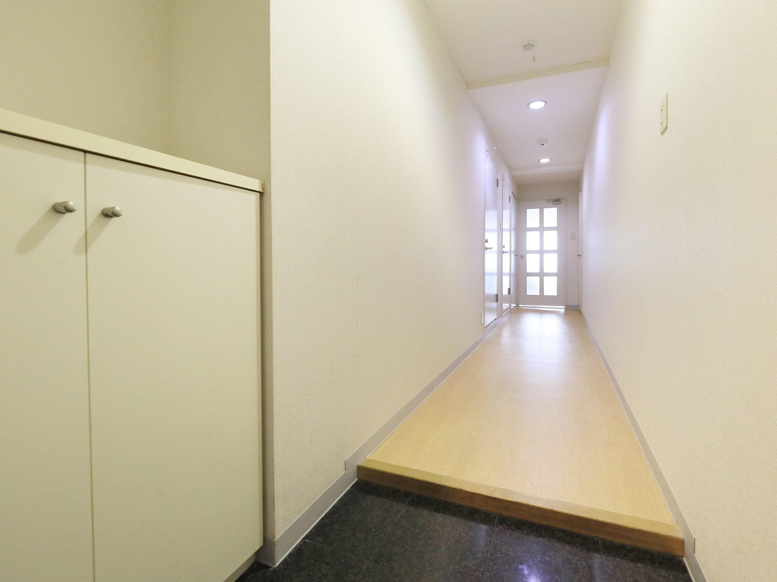A narrow hallway with a wooden floor, white walls, and a door at the end.