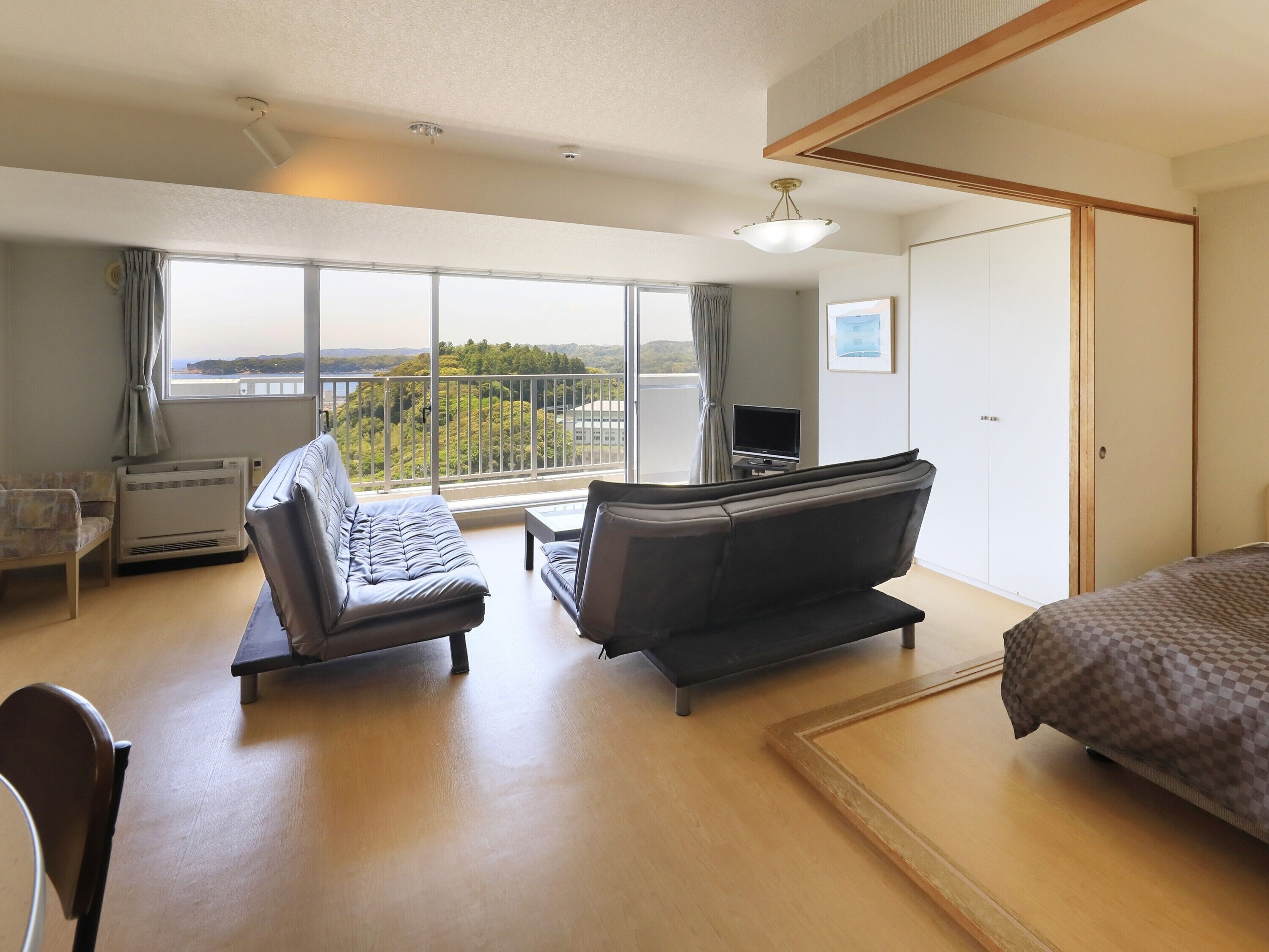 Une chambre d’hôtel avec un lit, deux canapés, un bureau, une télévision et un balcon avec vue.