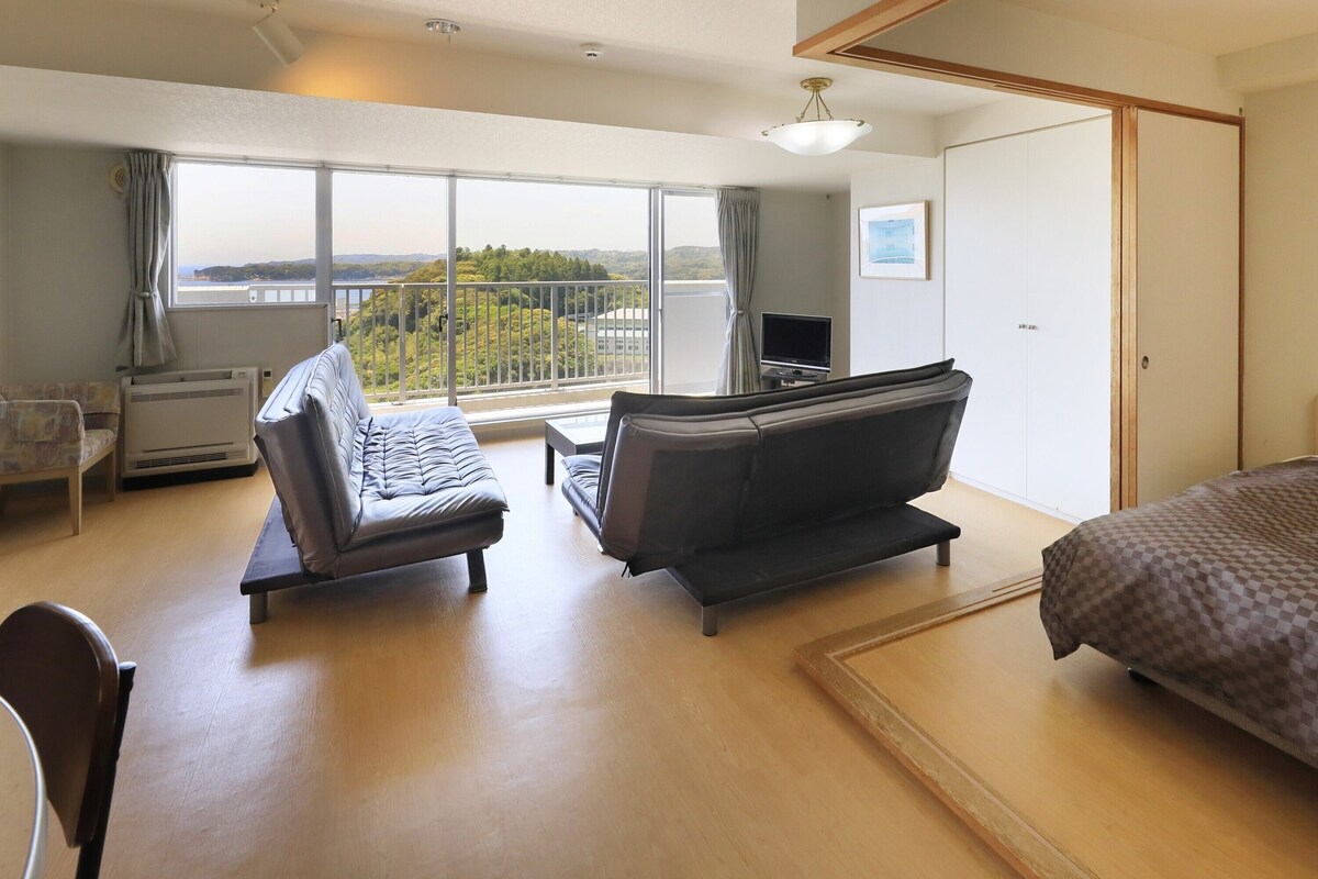 Une chambre d’hôtel avec un lit, deux canapés, un bureau, une télévision et un balcon avec vue.