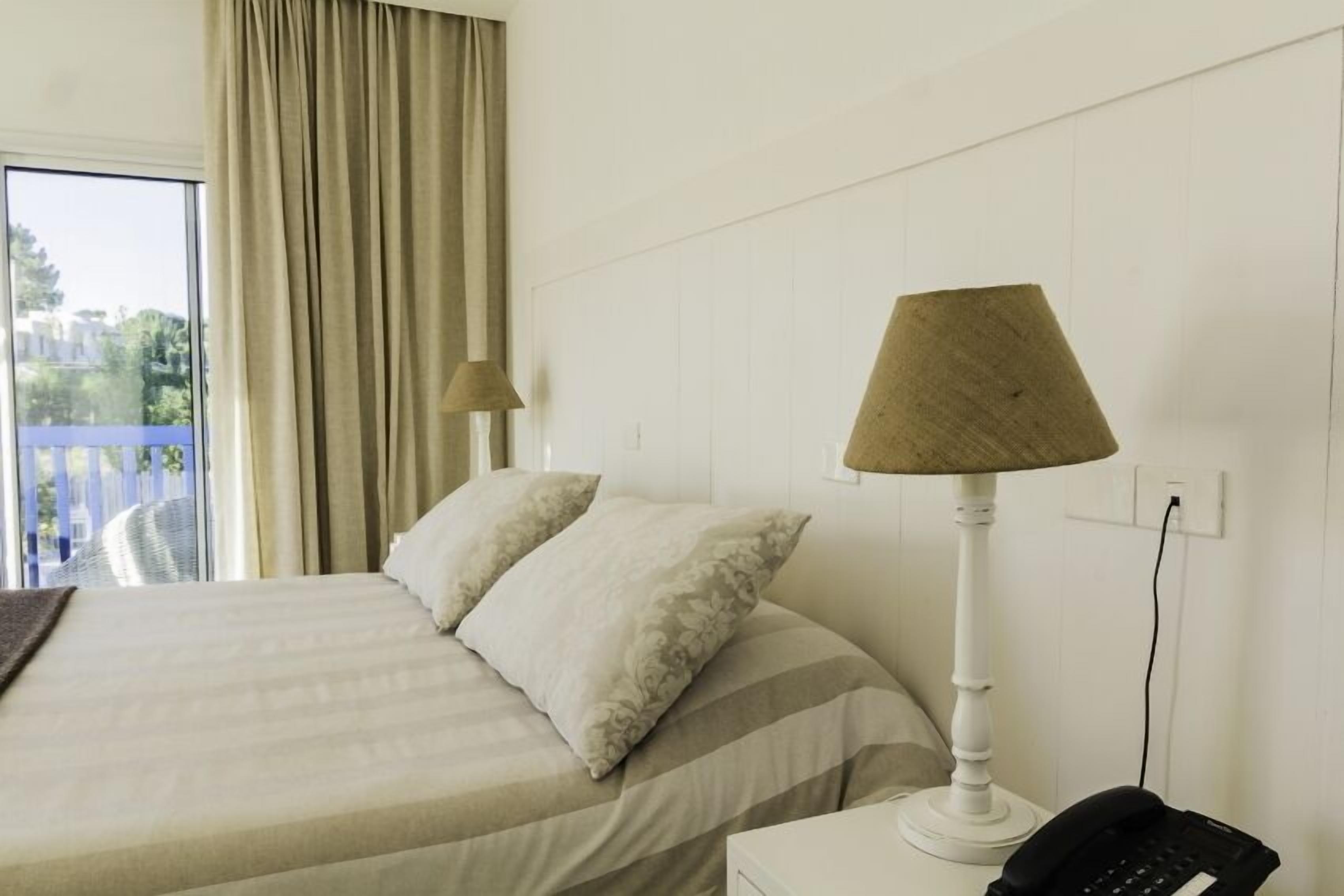 A hotel room with a bed, a lamp, a phone, and a view of the outdoors.