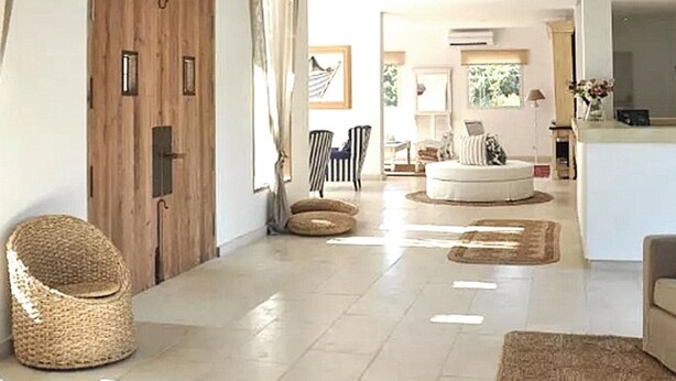 Un'ampia zona giorno con soffitto alto, una grande porta in legno e una poltrona in vimini.