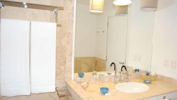Een badkamer met een beige betegelde muur, een witte wastafel, een grote spiegel en twee witte handdoeken aan een handdoekhouder.