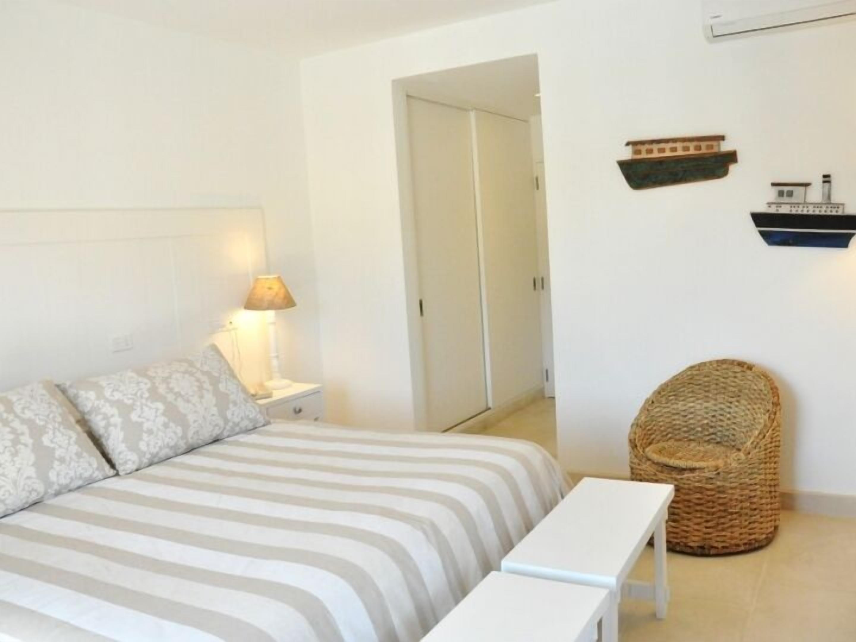 A bedroom with a bed, bedside table, lamp, and a wicker chair.