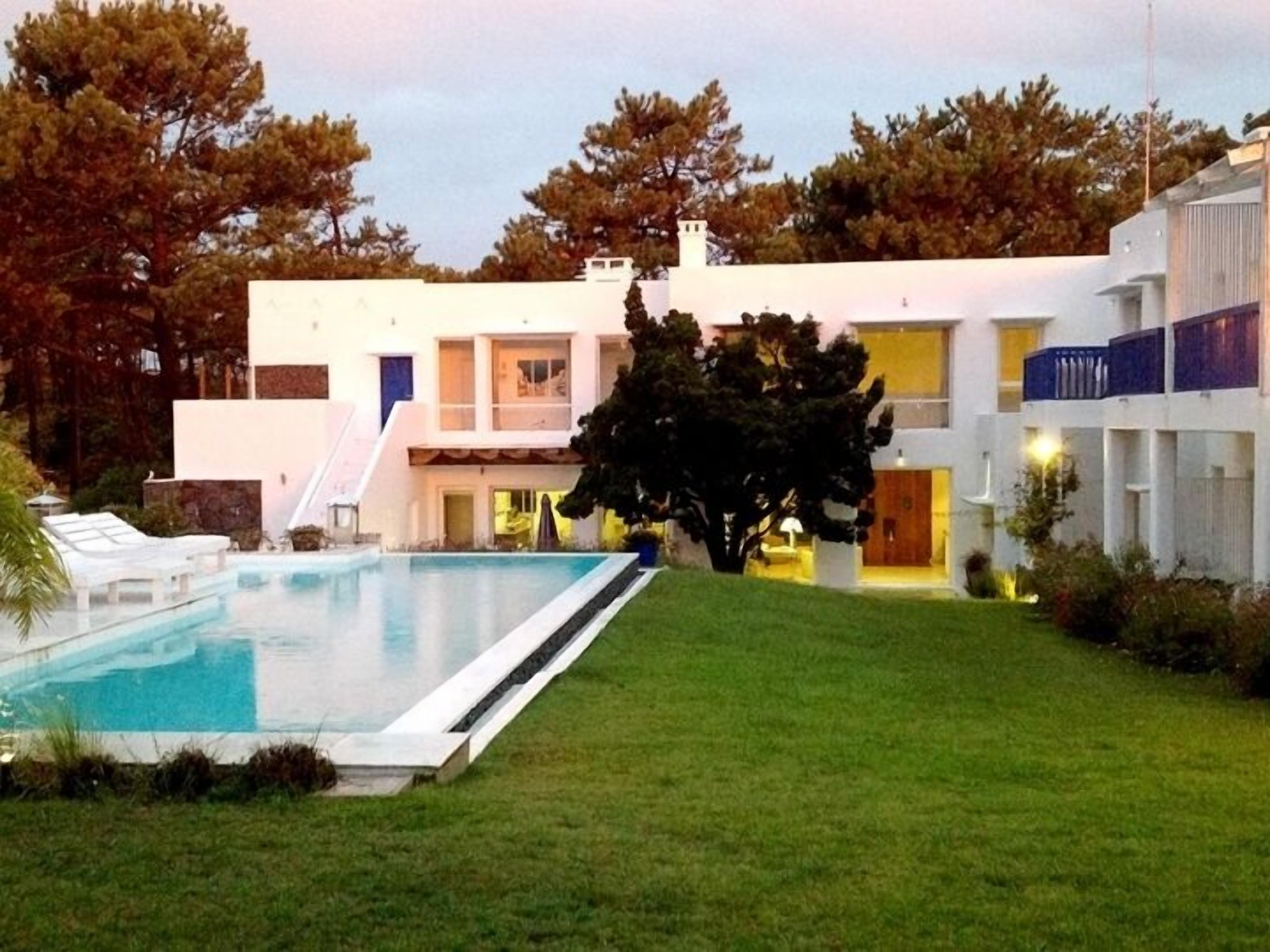 A modern two-story building with a swimming pool, a covered patio, and a large tree in the foreground.