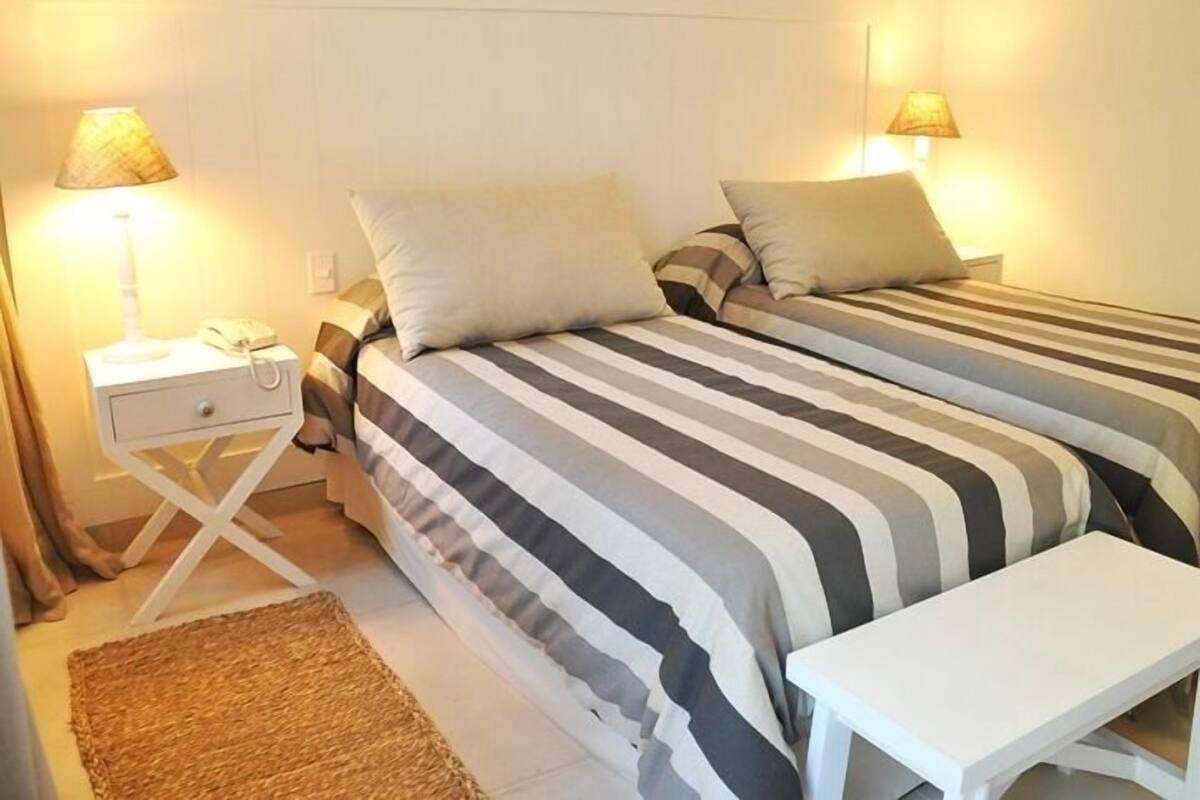 A double bed with striped bedding, a bedside table with a lamp, and a small bench.