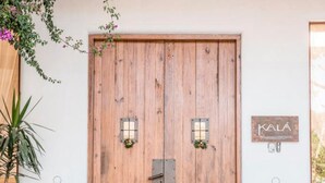 Una porta doppia in legno con un piccolo oblò e una chiusura in metallo. Sulla parete a destra, un cartello con la scritta "KALA".