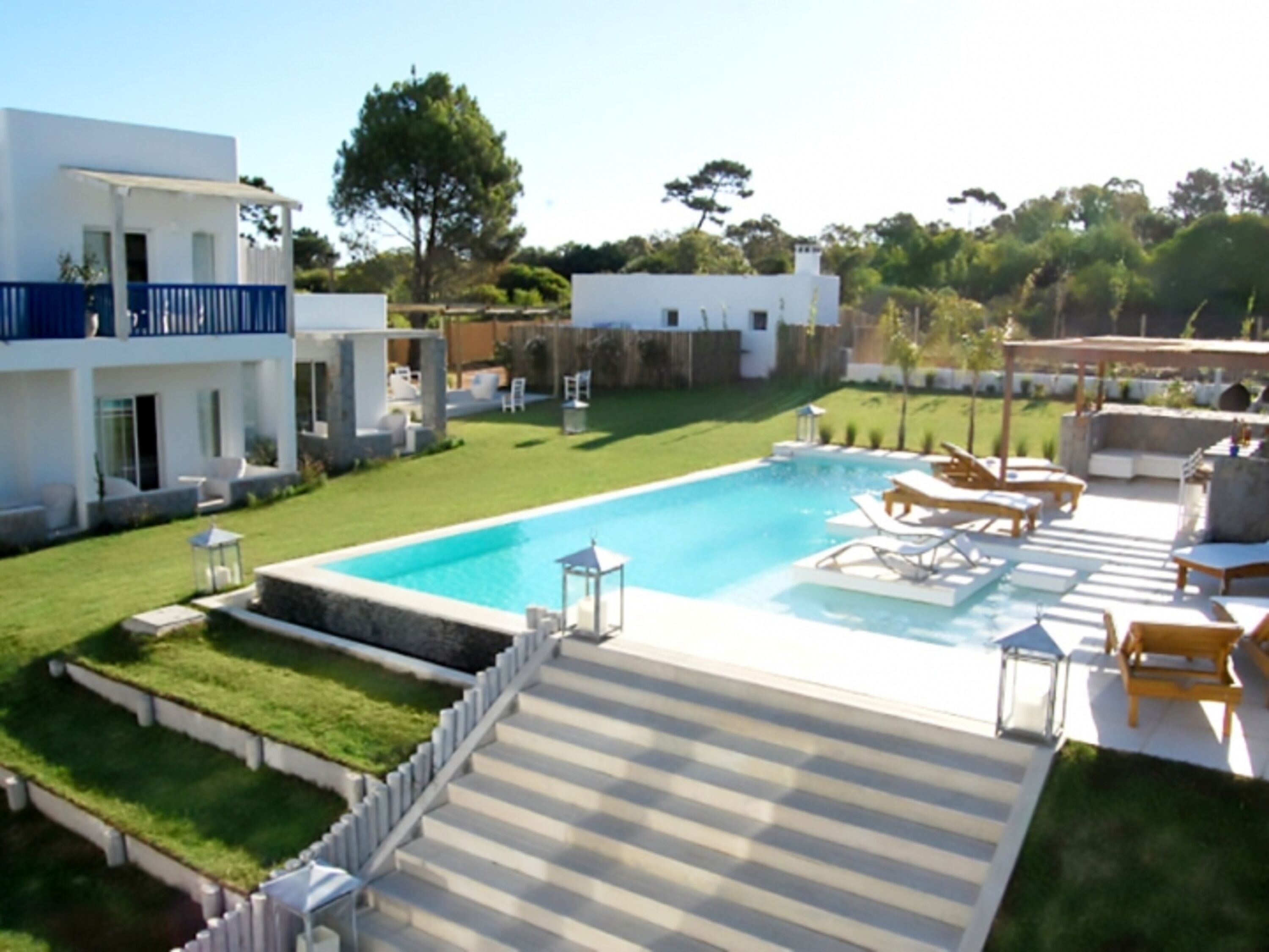 A modern pool area with a clear blue pool, sun loungers, and a well-maintained lawn.