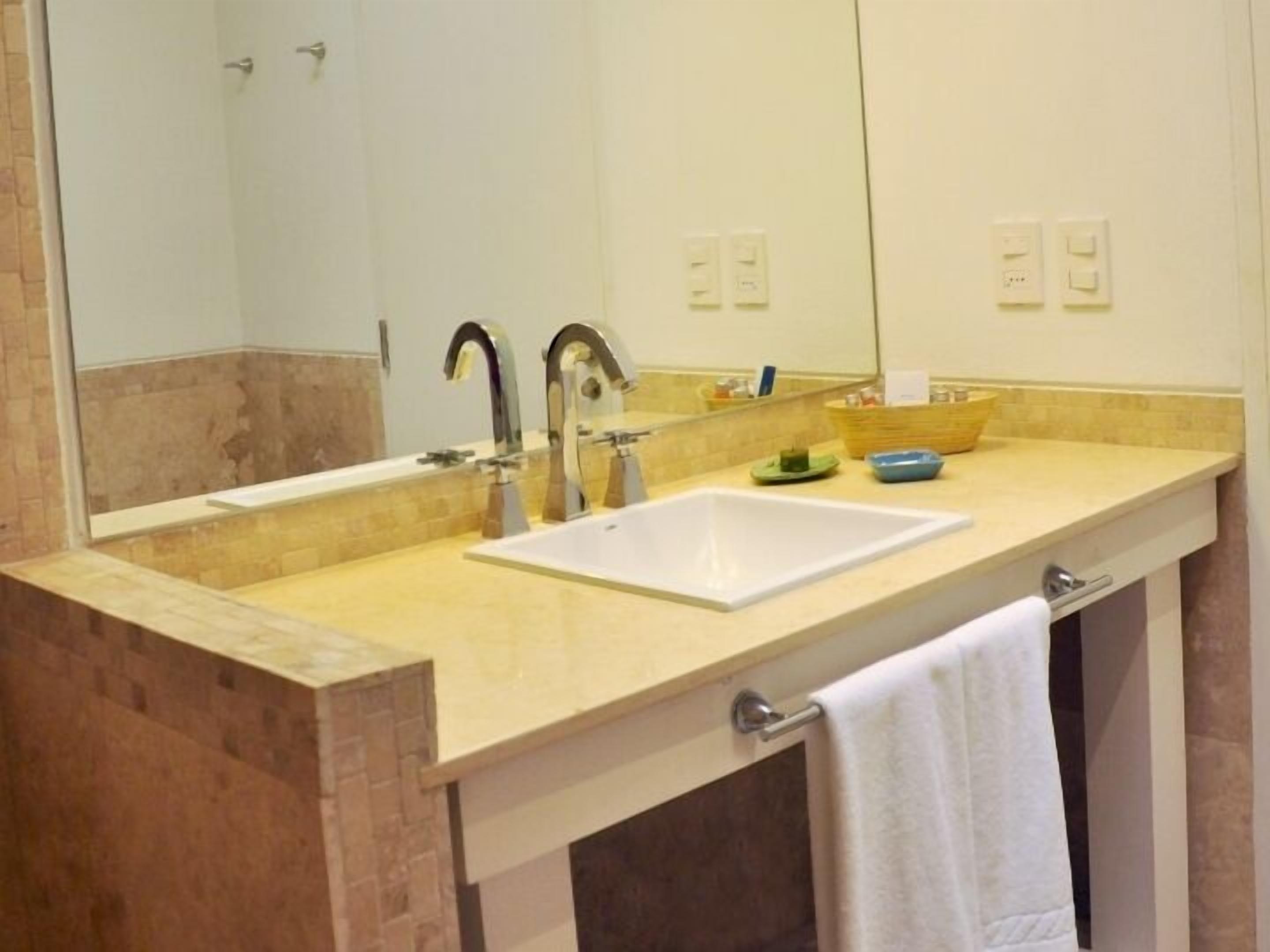 A bathroom with a white sink, two faucets, a mirror, and a towel rack.