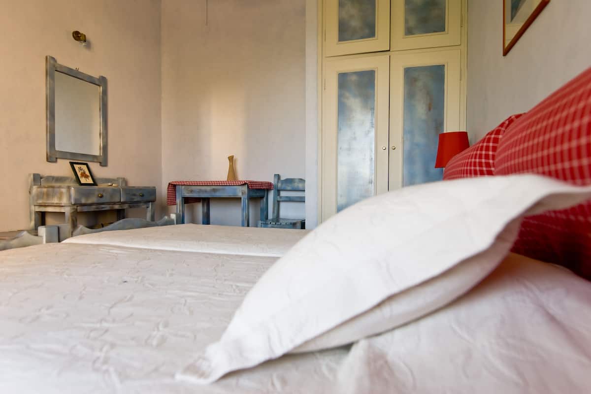 A bedroom with a bed, a dresser, a mirror, and a table with a red and white checkered tablecloth.