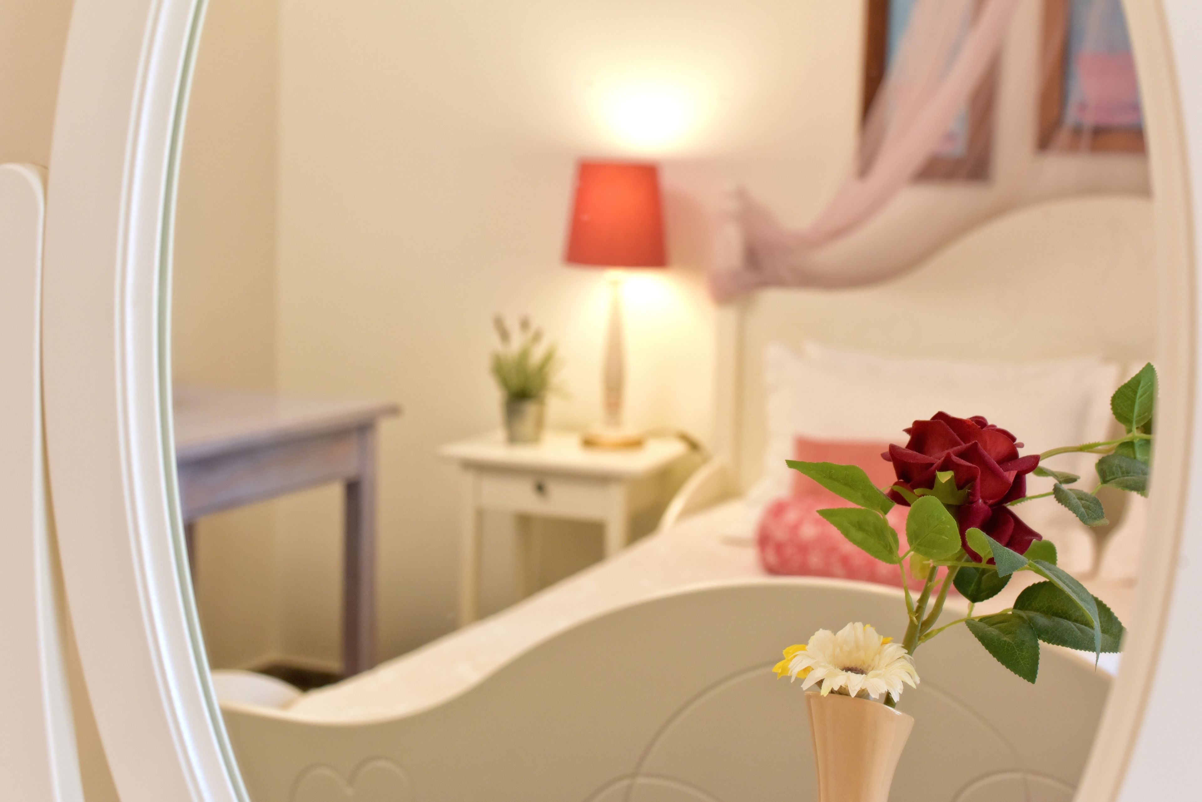 Ein Schlafzimmer mit einem Bett, einem Nachttisch, einer Lampe und einer Vase mit Blumen.