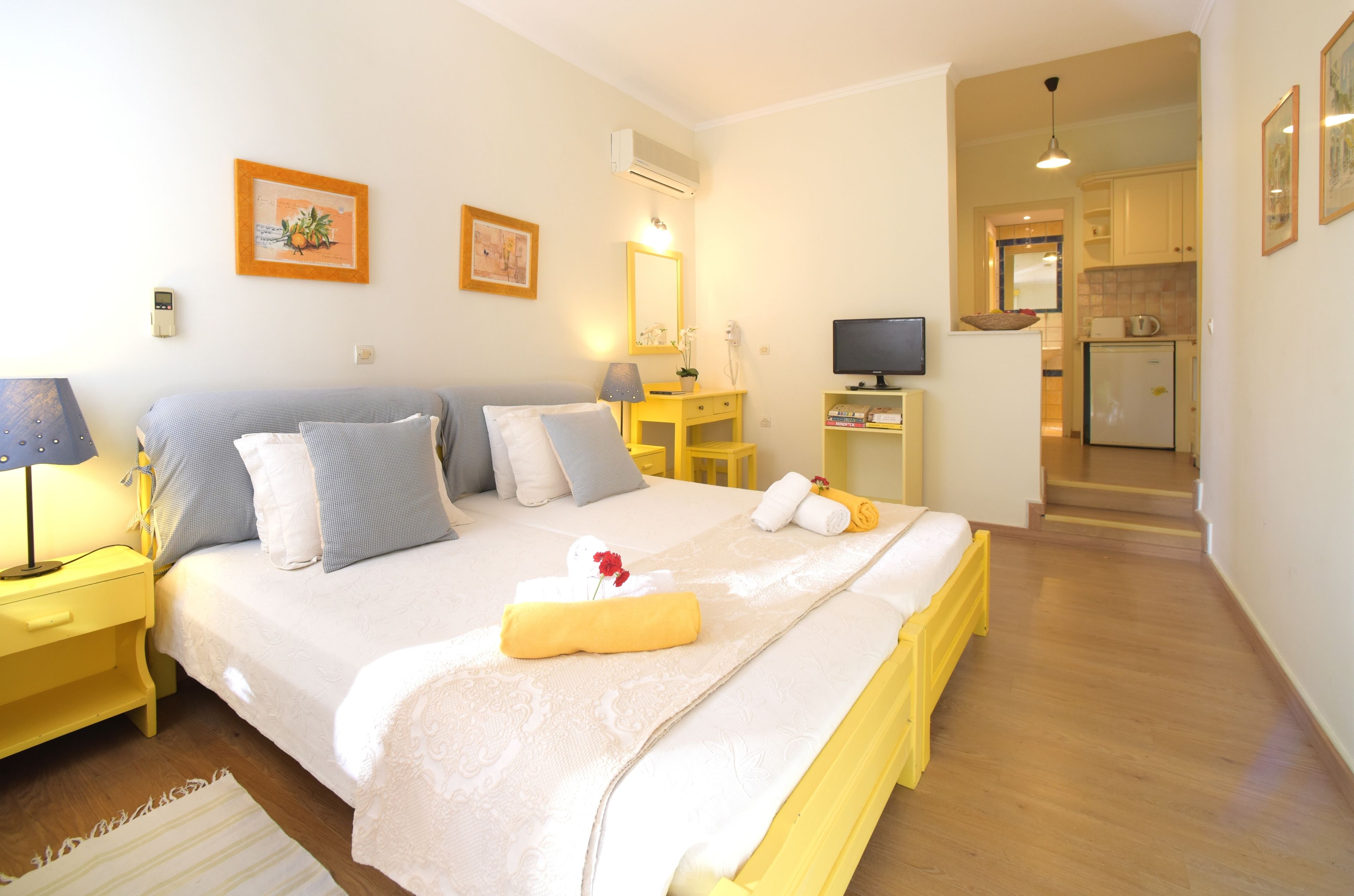 A well-lit bedroom with a large bed, bedside tables, a desk, and a television.