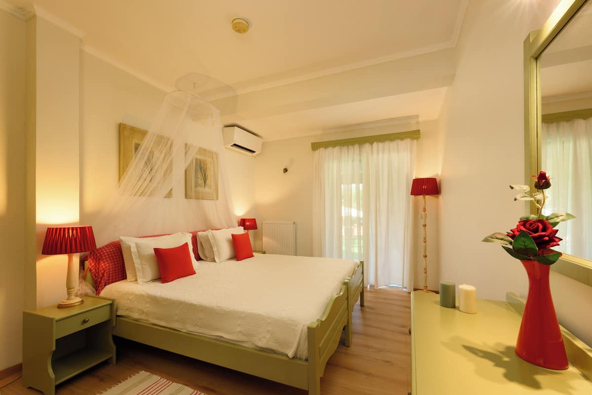 A neatly arranged bedroom with a bed, bedside table, lamp, mirror, and a vase with flowers.