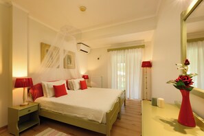 A neatly arranged bedroom with a bed, bedside table, lamp, mirror, and a vase with flowers. - Isabella Country House (Corfu)