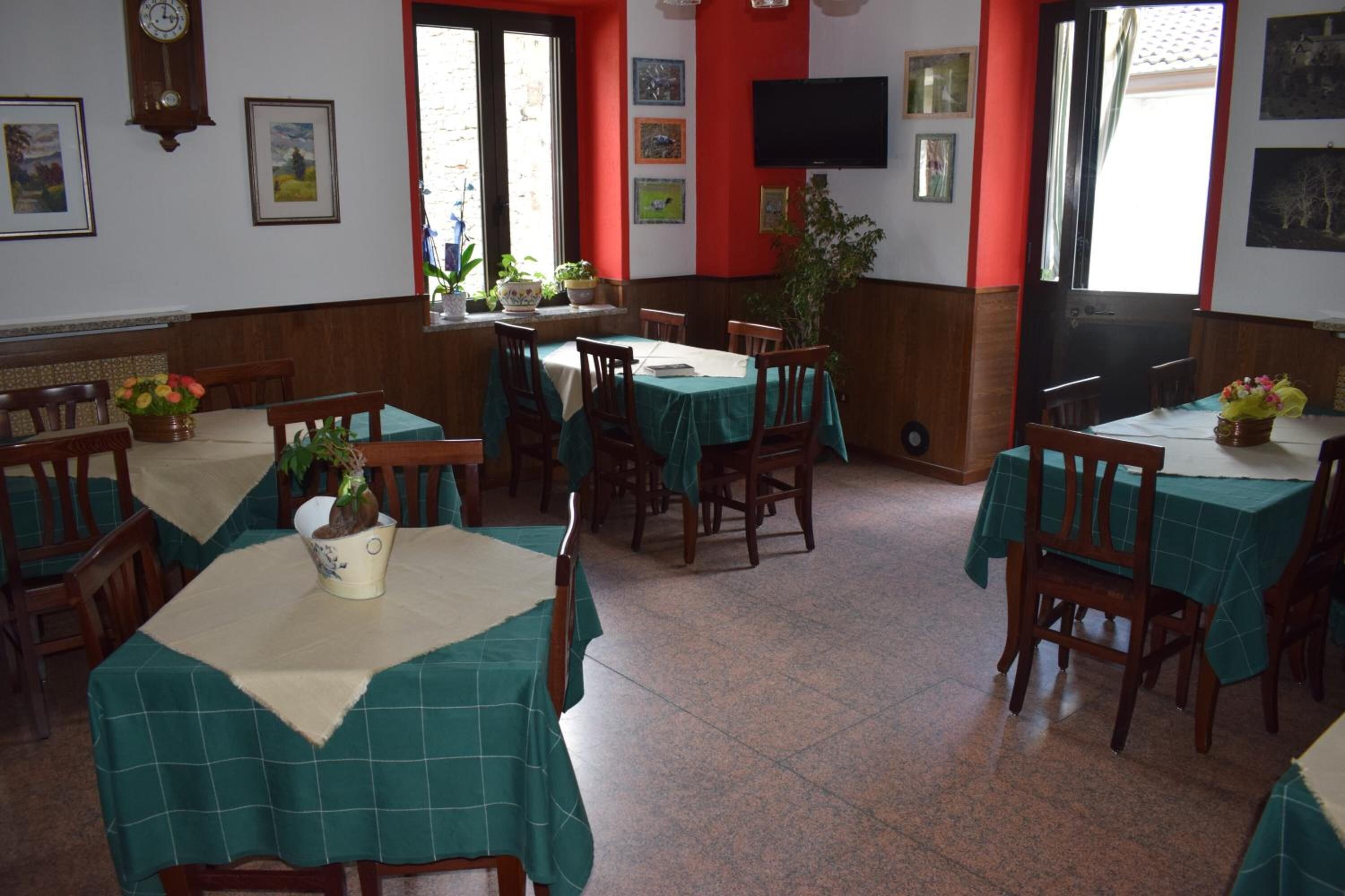 A dining area with multiple tables covered with green tablecloths, wooden chairs, and potted plants.