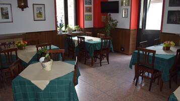 Zona pranzo con diversi tavoli ricoperti da tovaglie verdi, sedie di legno e piante in vaso.