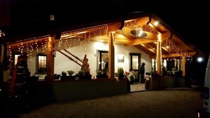 A building with a covered outdoor area, string lights, and a Christmas tree. - Albergo Canella (Fuipiano Valle Imagna)