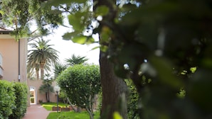 Un chemin menant à un bâtiment agrémenté d’un palmier et d’un jardin bien entretenu.