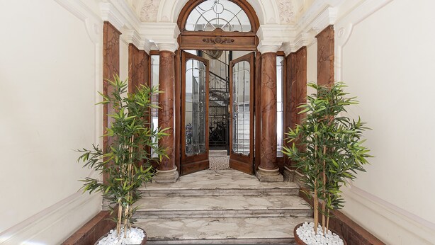 A grand entrance with marble steps, wooden doors, and two potted plants. - Residenza Zanardelli (Rome)