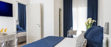 Une chambre d’hôtel avec un lit, un bureau et une chaise, une télévision et une fenêtre avec des rideaux.