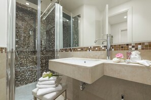 A bathroom with a glass-enclosed shower, a sink with toiletries, and a stack of towels. - Residenza Zanardelli (Rome)