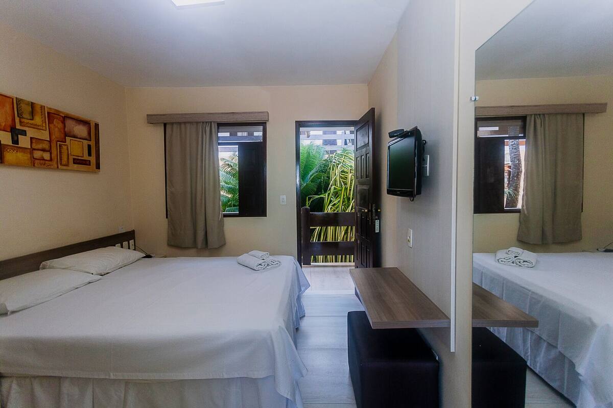 Ein Hotelzimmer mit zwei Betten, einem Fernseher und Blick auf Grünflächen.