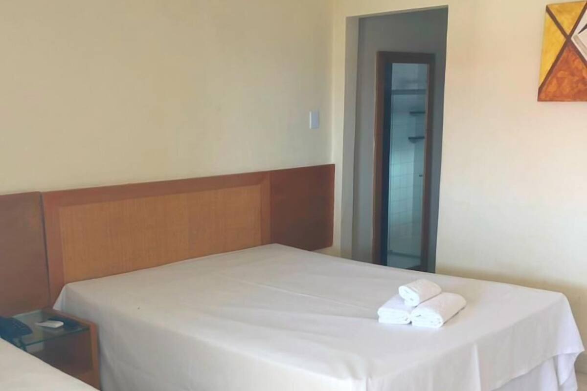 Ein Hotelzimmer mit zwei Betten, einem Holzkopfteil, einem kleinen Nachttisch und einem Spiegel an der Wand.