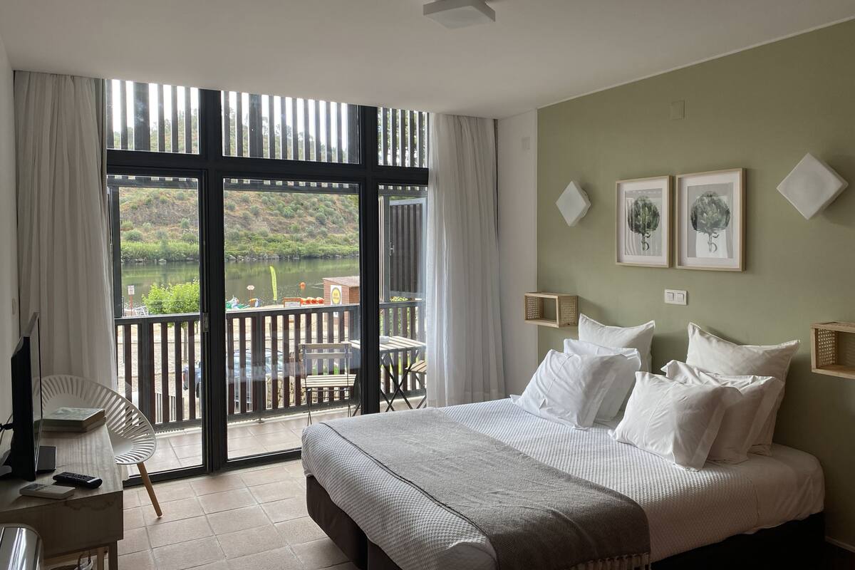 Un dormitorio con una cama grande, un escritorio con una silla y vistas a un lago a través de una puerta corredera.