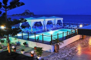 A pool area with lounge chairs and a covered seating area, surrounded by potted plants and a view of the sea. - Sacallis Inn Beach Hotel (Kos)