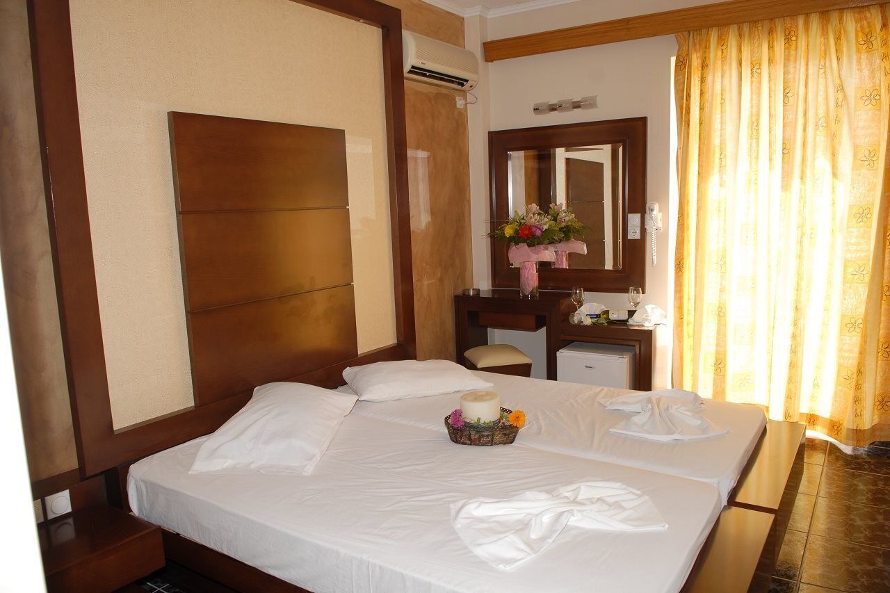 A hotel room with a large bed, a wooden headboard, a small desk, a mirror, and a window with curtains.