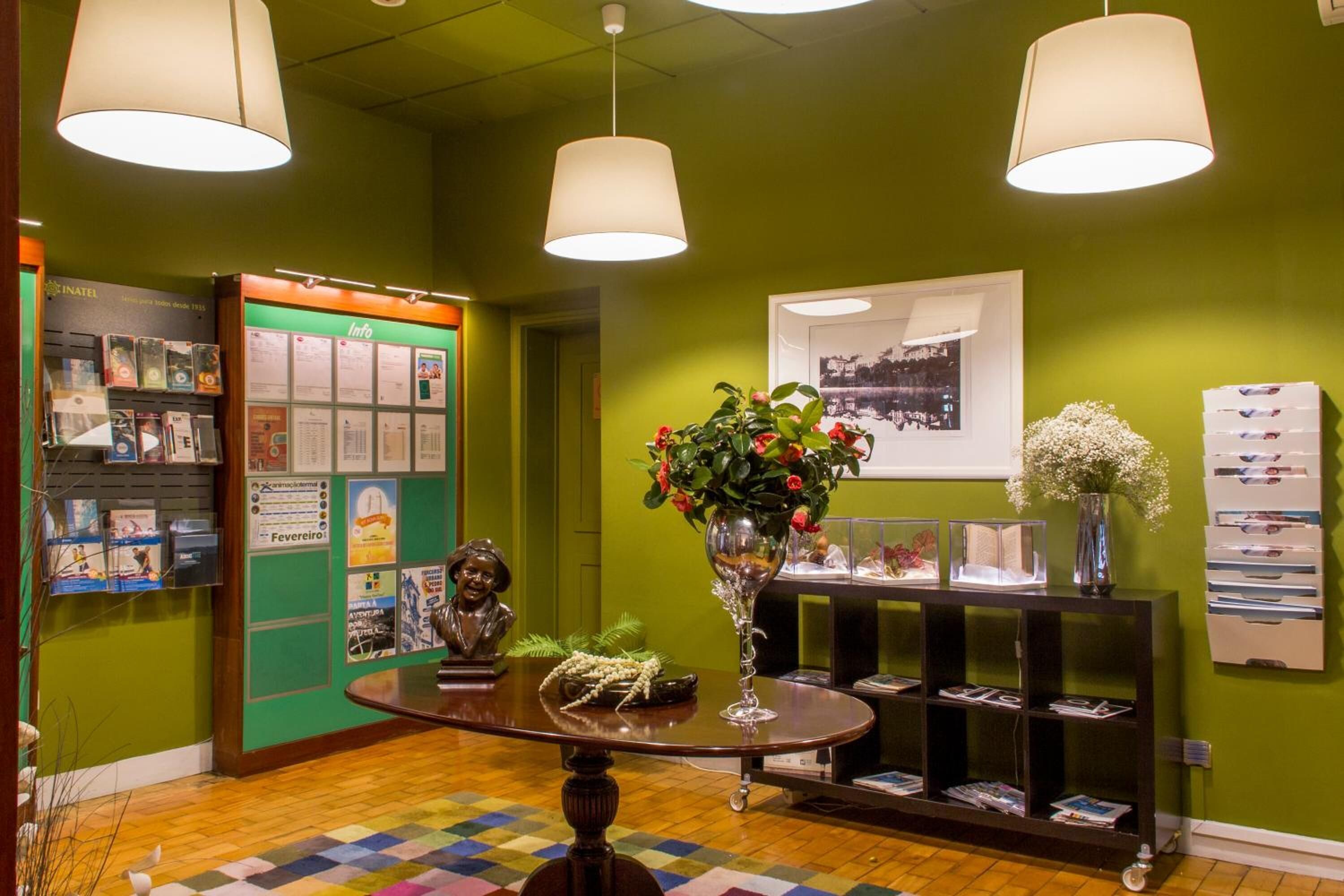 A lobby with a green wall, a bulletin board, a round table with a vase of flowers, and a bookshelf.