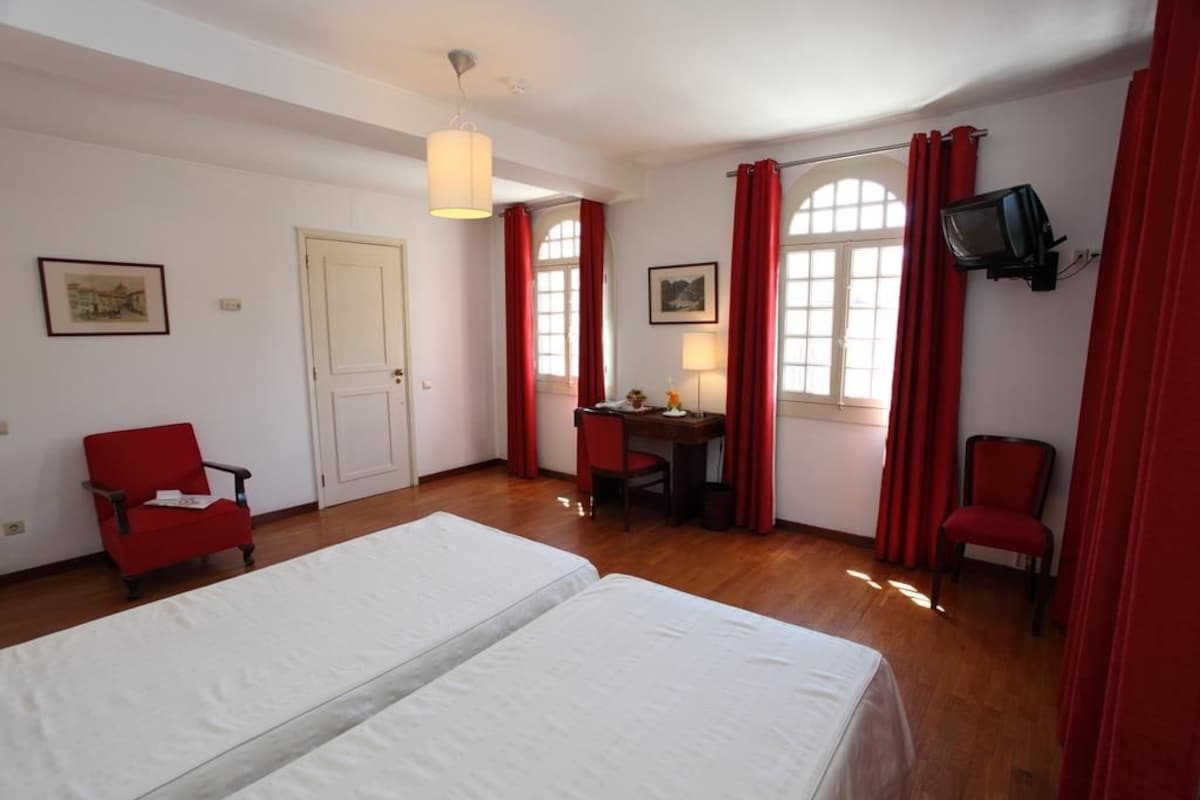 Une chambre d’hôtel avec deux lits, un bureau, une chaise et un téléviseur.