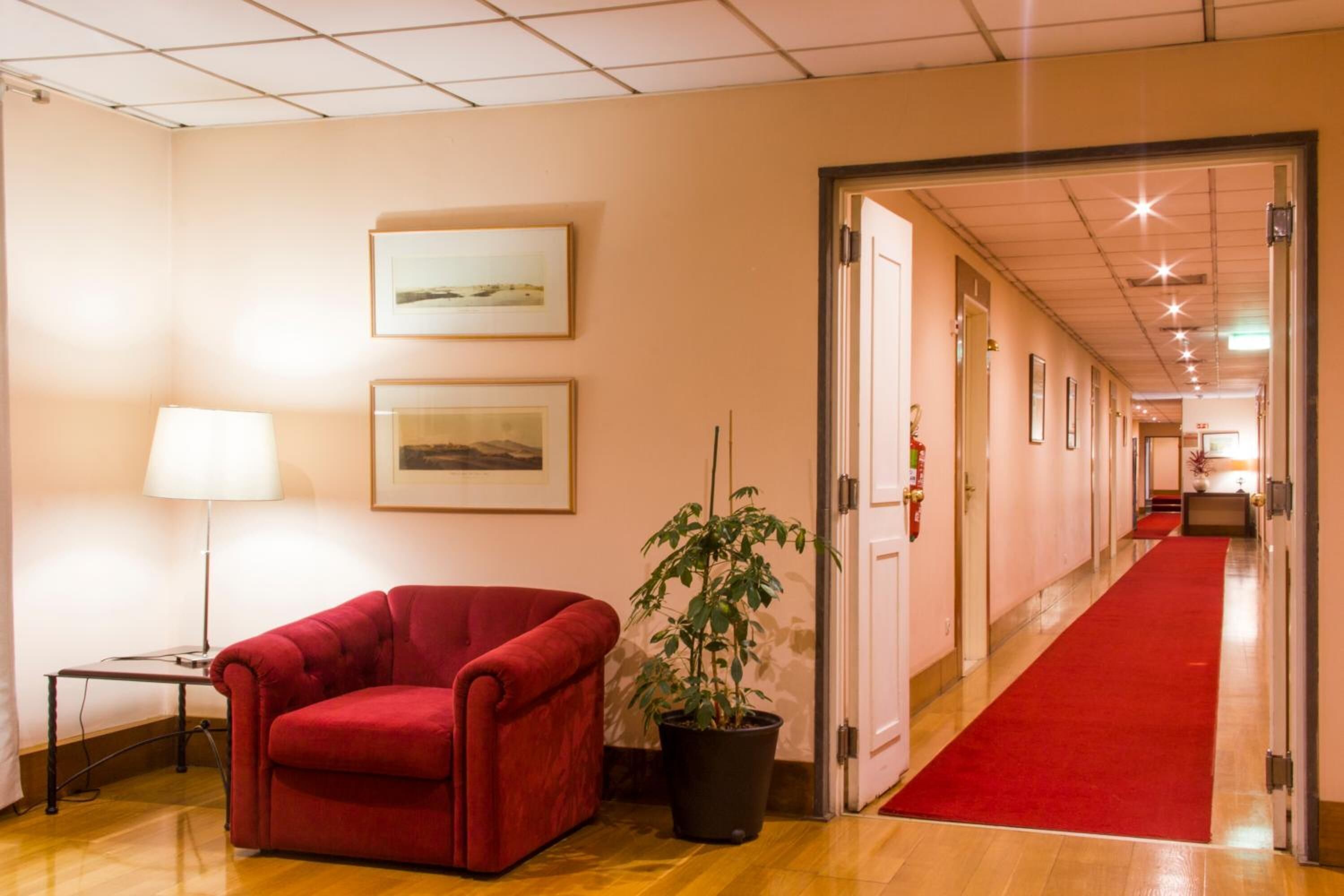 Un hall d’hôtel avec un fauteuil rouge, une lampe sur pied et une plante en pot.