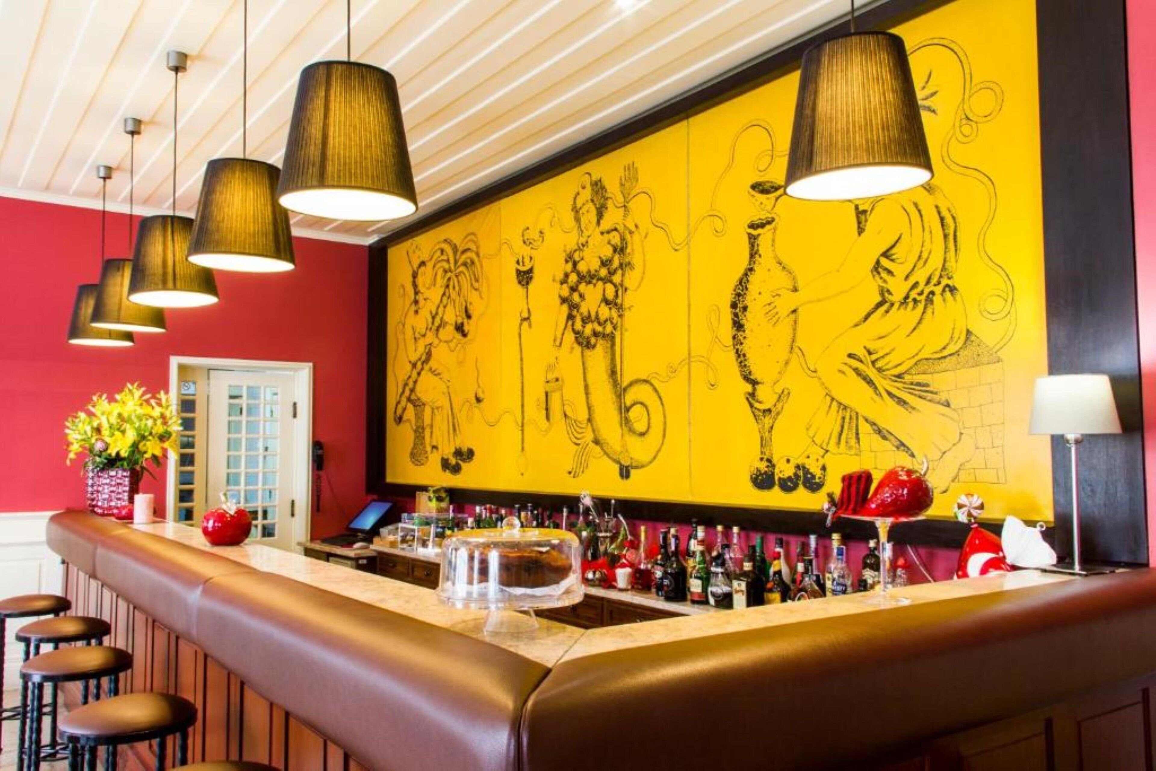 Una zona de bar con una barra larga, varias lámparas colgantes y un gran mural amarillo en la pared.