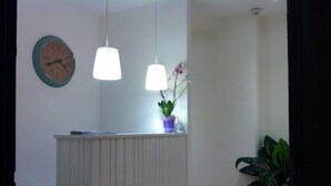 A reception area with a white reception desk, two pendant lights, a clock, and a potted plant. - B&B Medinblu Via Miraglia (Reggio Calabria)