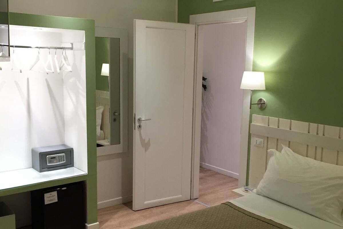 A bedroom with a bed, a bedside table, a mirror, a wardrobe, and a lamp.