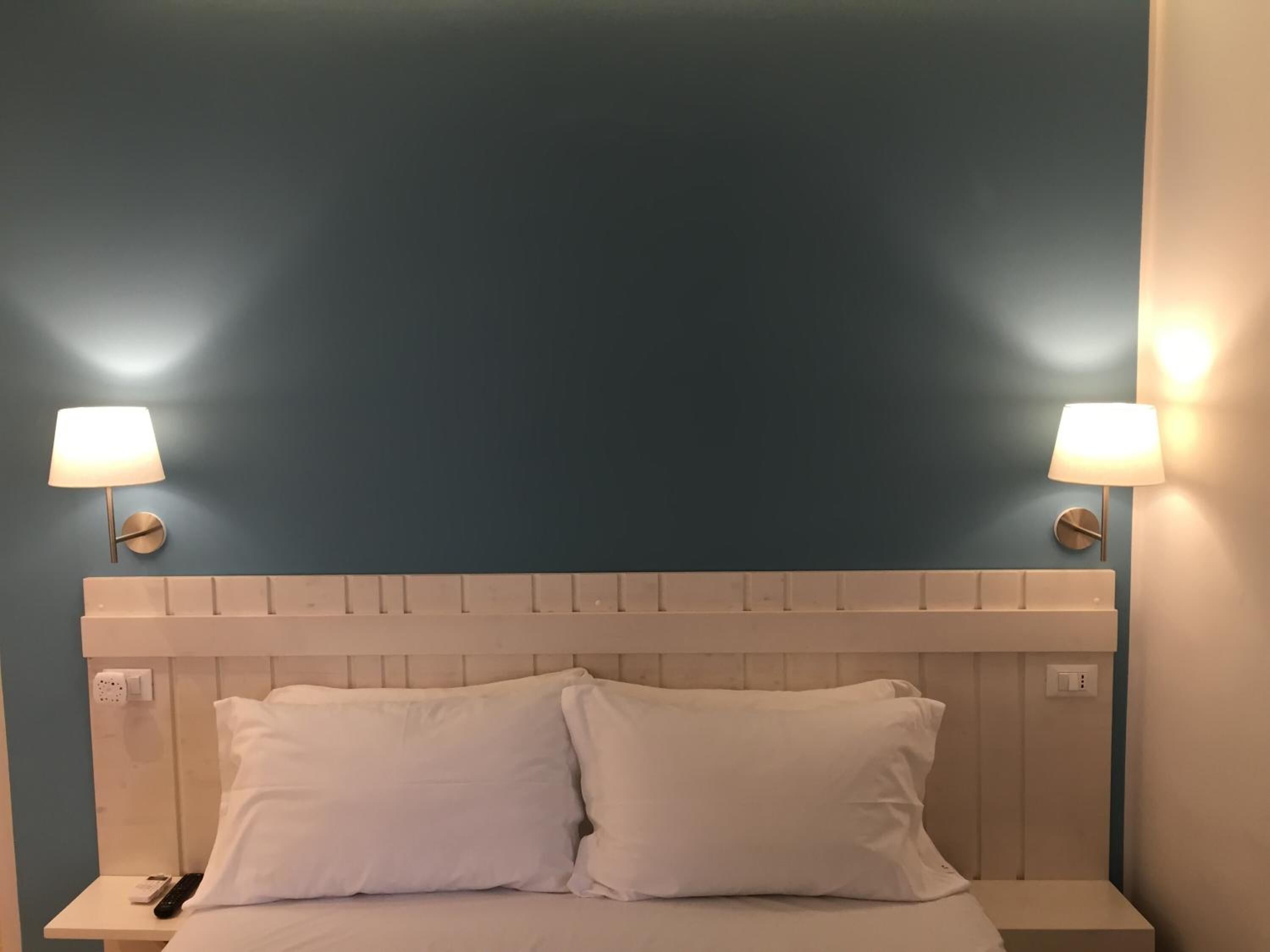 A hotel room with a blue accent wall, a white headboard, and two bedside lamps.