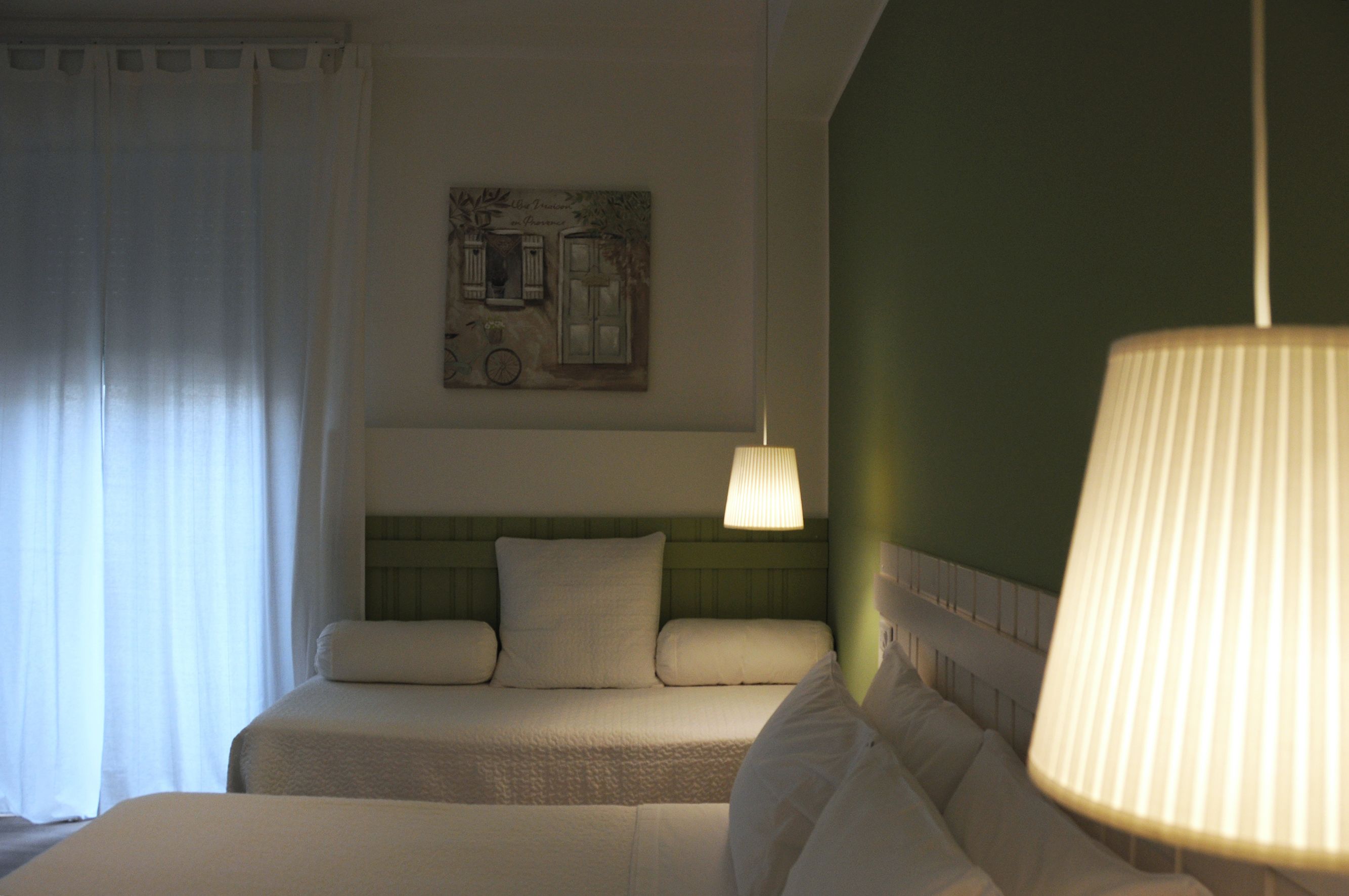 A hotel room with a bed, a headboard, a wall-mounted artwork, and a hanging lamp.
