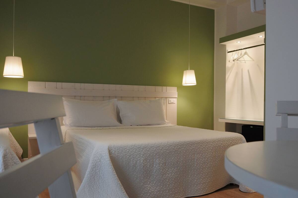 A neatly made bed with white linens, a white headboard, and two hanging pendant lights.