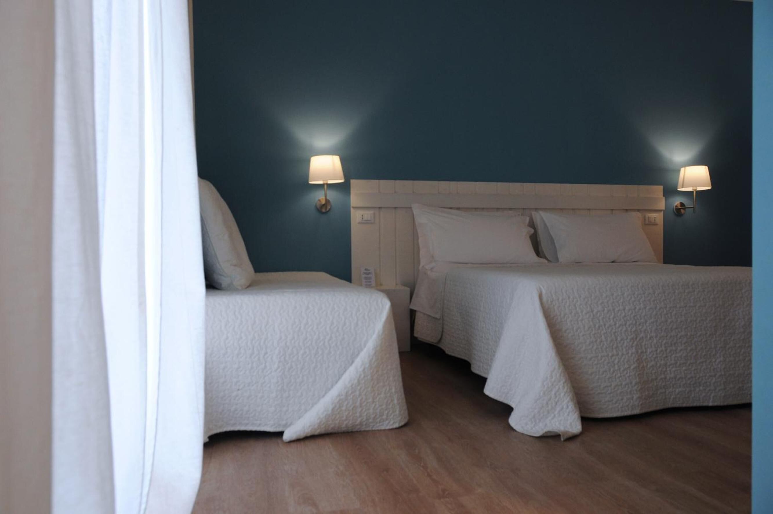 A hotel room with two beds, white bedding, and wall-mounted lamps.