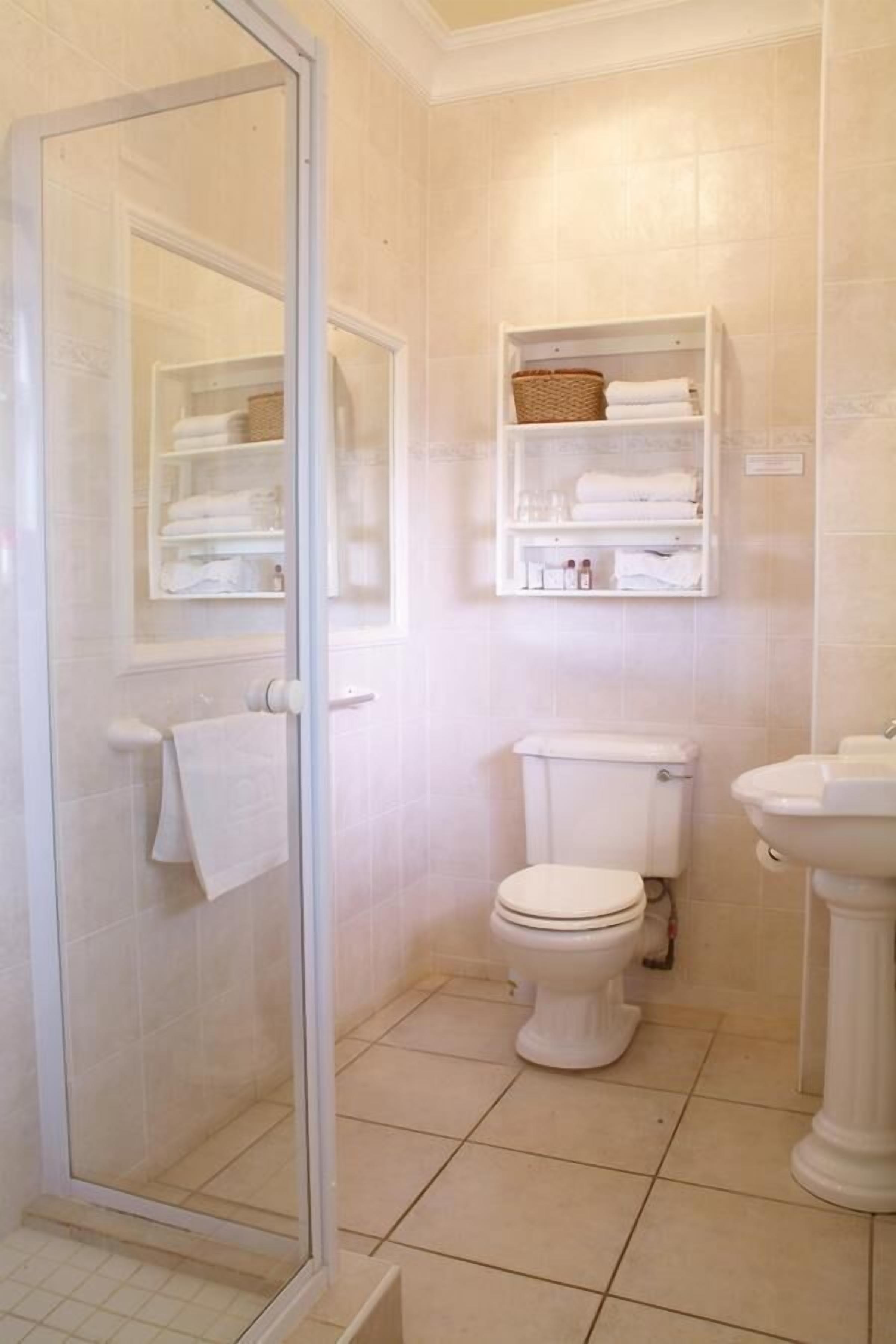 Un baño con cabina de ducha de vidrio, inodoro, lavamanos y estante con toallas y artículos de aseo.