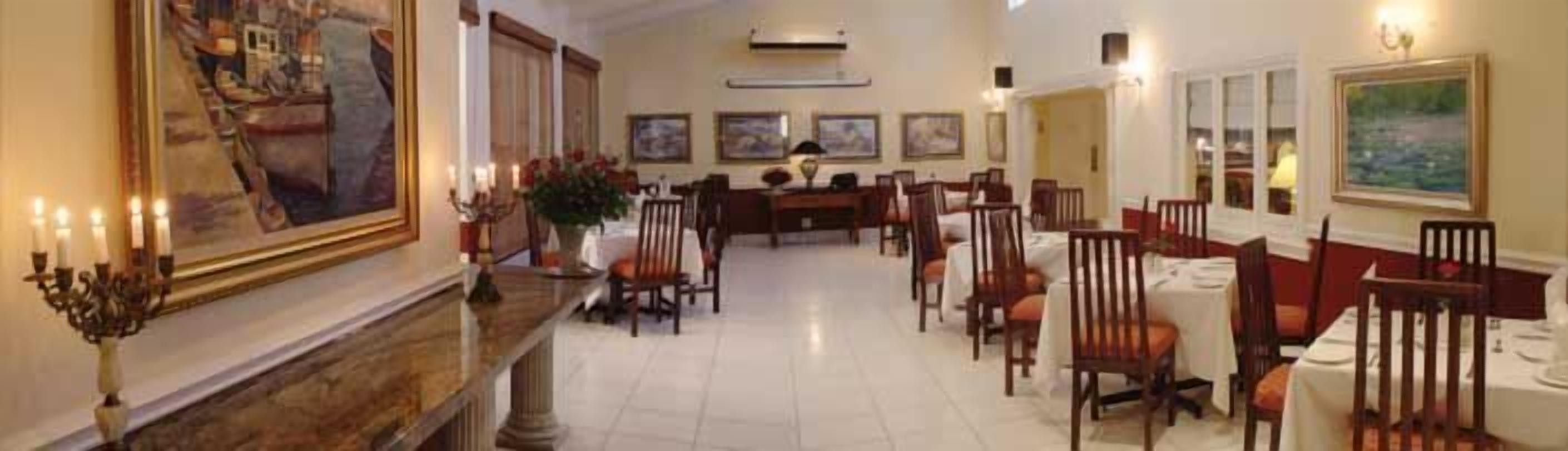 Ampla sala de jantar de hotel, com uma mesa comprida, diversas cadeiras e um candelabro.
