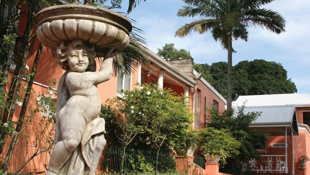 Une statue représentant une figure tenant un grand bol, un espace d’accueil et un bâtiment orné de colonnes.