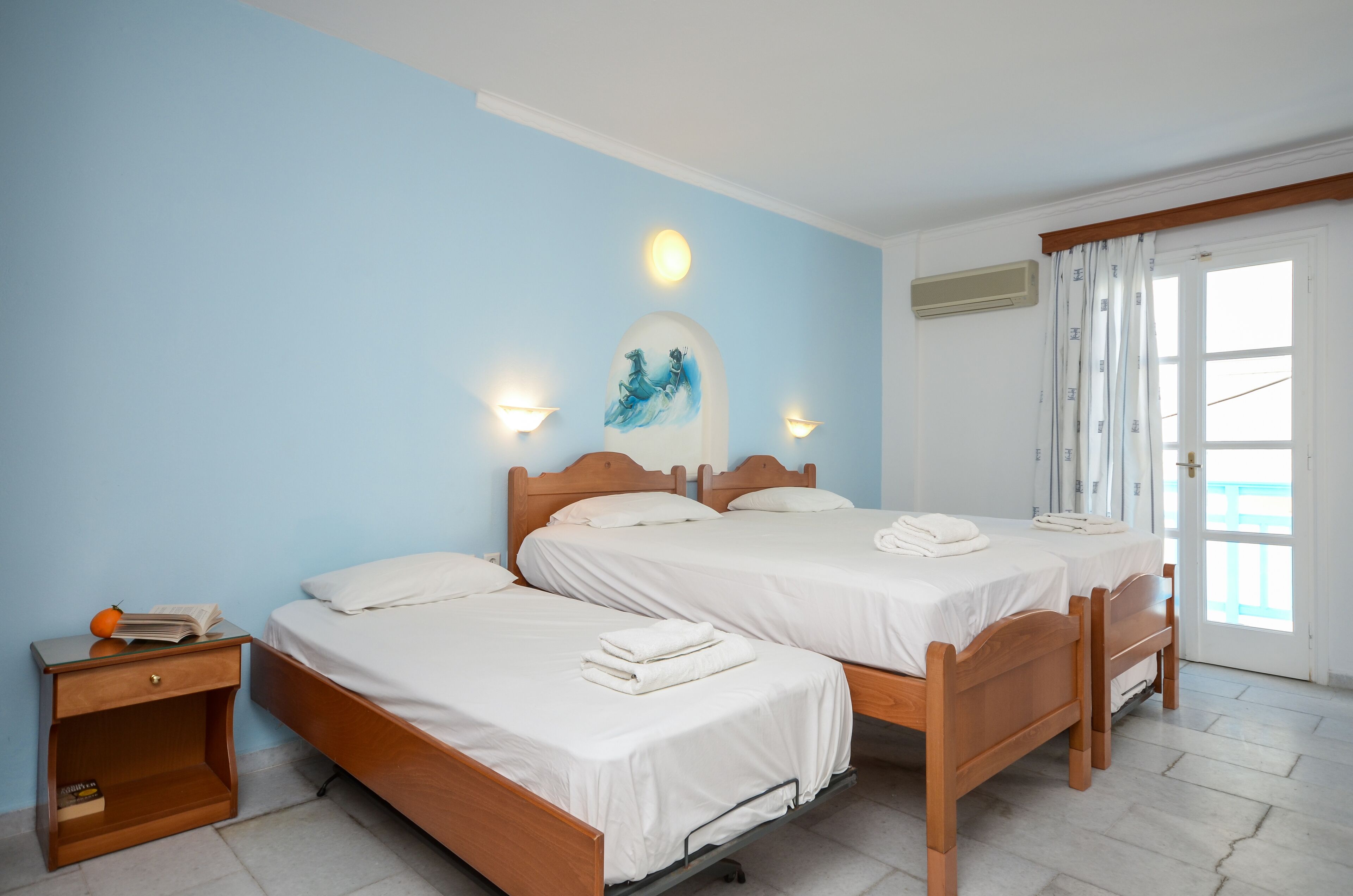 A hotel room with two wooden beds, white bedding, a nightstand with a phone and books, and a painting on the wall.