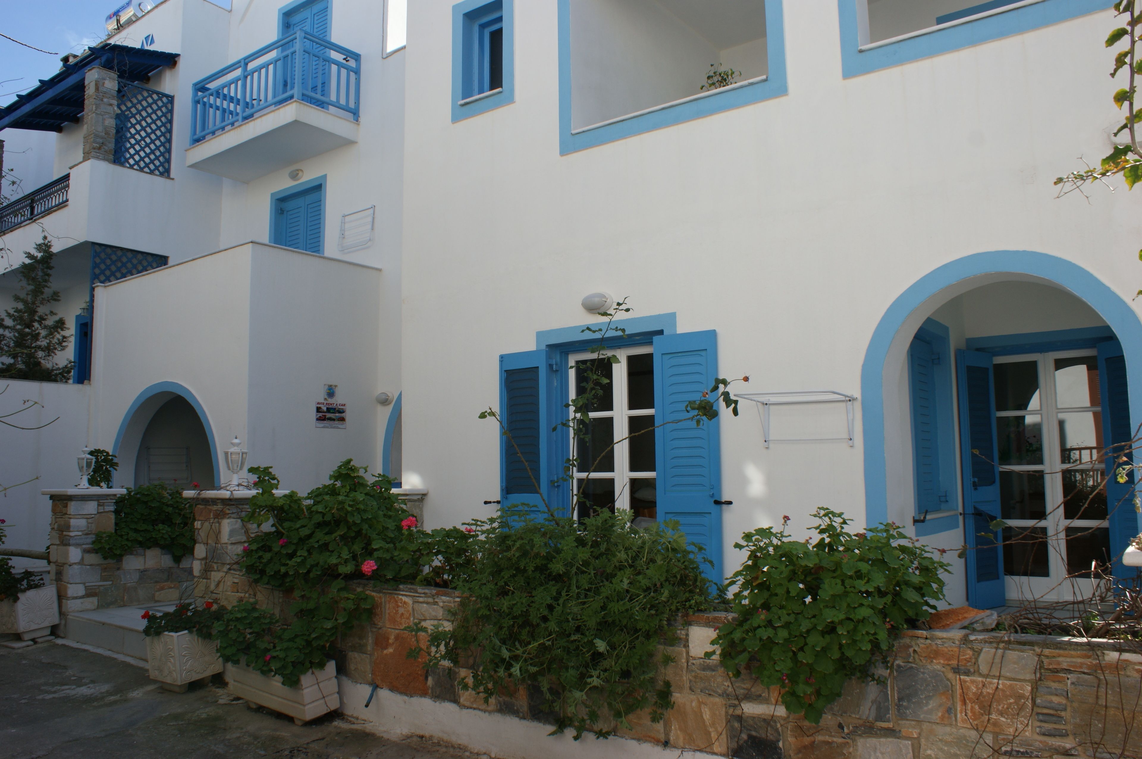 A white building with blue shutters and balconies, stone steps, and potted plants.