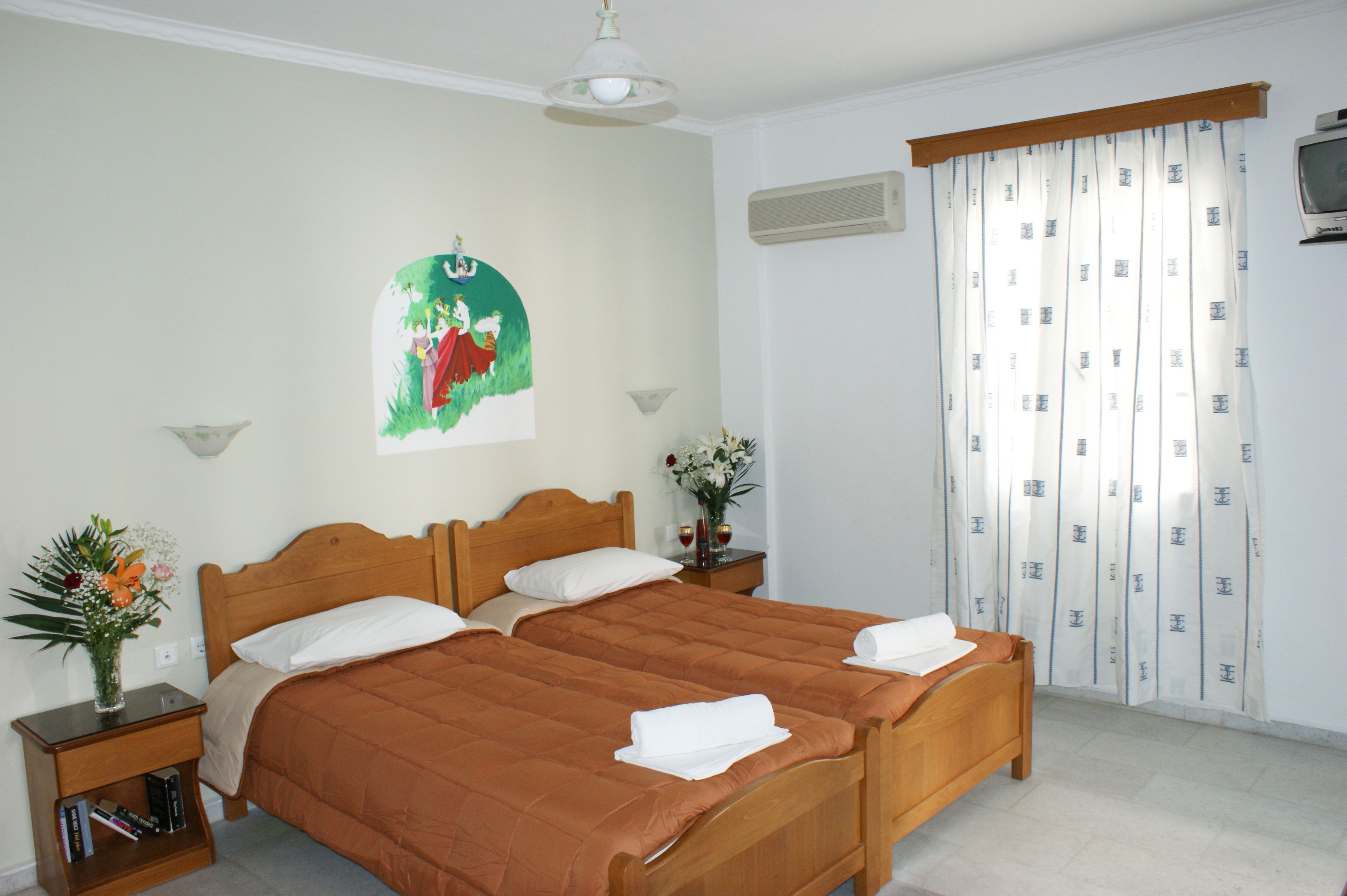 A double bed with a brown quilt, a nightstand with a vase of flowers, and a painting on the wall.