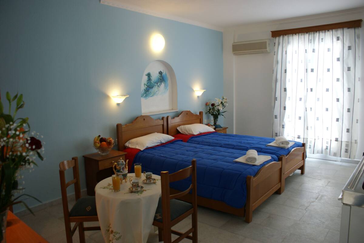 A hotel room with a large bed, two bedside tables, a small table with a vase of flowers, and a window with curtains.