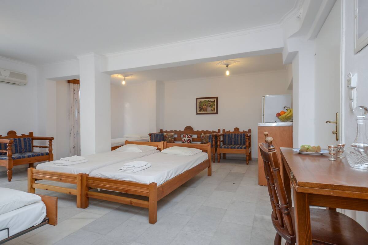 A hotel room with two wooden beds, a dining table, and a kitchen area with a refrigerator and fruit bowl.