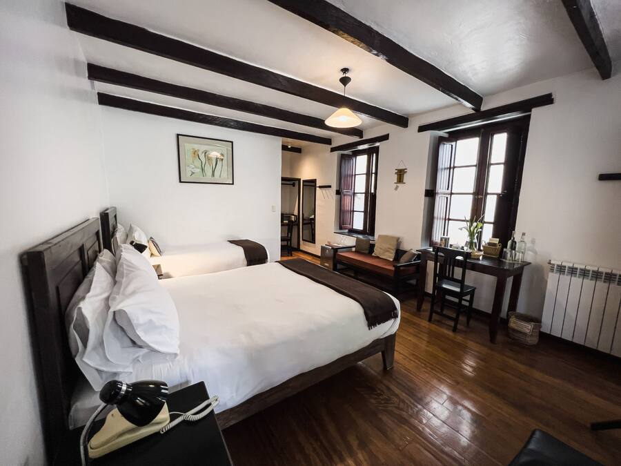 A hotel room with a large bed, a desk, and a chair. There is a window with a view of the outside.
