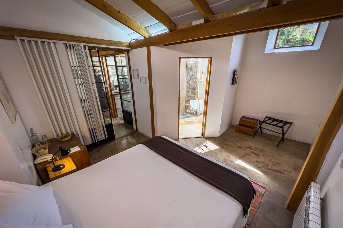 Een slaapkamer met een groot bed, een houten plafond, een klein tafeltje en een raam.